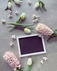 A blank blackboard picture frame surrounded by fragrant spring flowers, white tulips and pink...