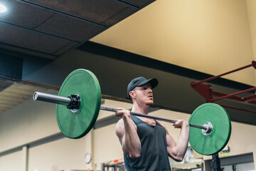 Red-haired athlete in cap, performing shoulder press with barbell.