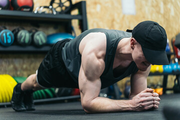 Young athlete in cap, doing plank exercise, muscles tense.