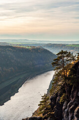 Water flows through a valley, embraced by towering mountains and lush trees, creating a stunning natural landscape under the open sky