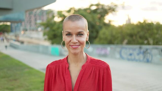 Cheerful adult woman with shaved hair smiling to camera at sunset