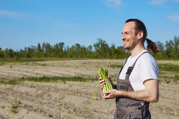 Happy farmer with bunch of green asparagus on field background - 757582819