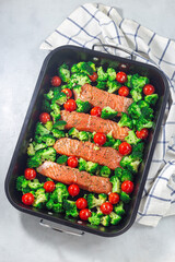 Raw salmon fillet with broccoli and tomato on frying tray, ready to bake, vertical, top view