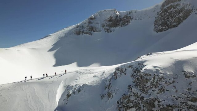 Aerial view of a group of alpinists walking on snow-covered mountain. They wear helmets and safety equipment. Mountaineering, climbing, alpinism concept.