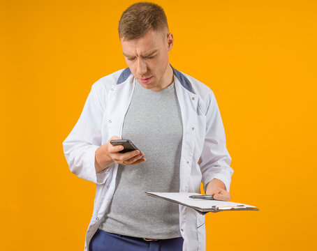 A medical professional distracted by his phone while holding a clipboard, against an orange backdrop.