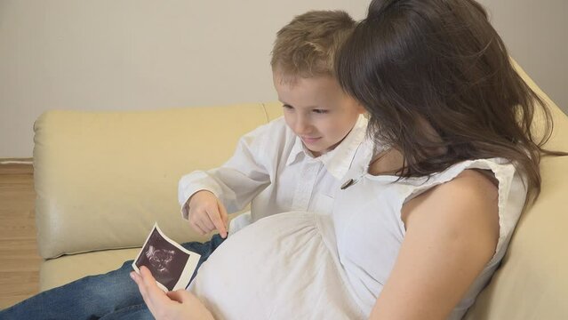 Mother showing to her son her pregnant belly and the ultrasound picture