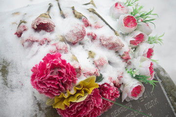Flowers on the grave. Artificial flowers at the cemetery. Snow on the buds.