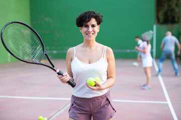 Portrait of positive latin woman frontenis player standing on outdoor fronton, holding racket and...