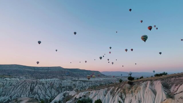 Colorful balloons in Cappadocia at dawn, flying in the sky over deep canyons. A lot of balloons with tourists are hanging and flying in the blue sky above the valley of rocks. Goreme, Turkey.
