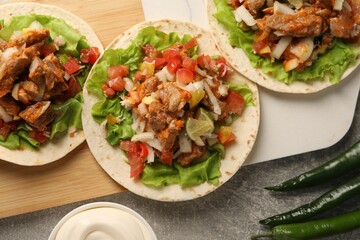 Delicious tacos with vegetables and meat on grey textured table, flat lay