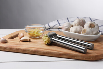 One metal press and garlic on white wooden table