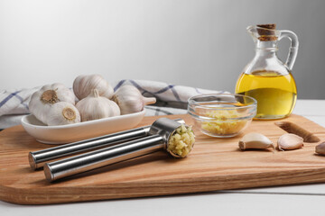 One metal press and crushed garlic on white wooden table