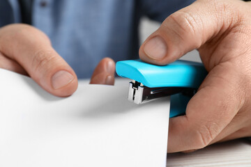 Man with papers using stapler at white table, closeup