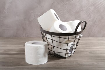Soft toilet paper rolls in metal basket on wooden table, closeup