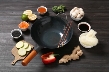 Empty iron wok and chopsticks surrounded by ingredients on dark grey wooden table