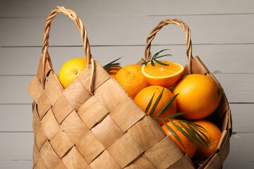 Wicker basket with whole and cut ripe oranges on wooden background, closeup