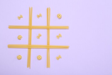 Tic tac toe game made with different types of pasta on lilac background, top view