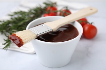 Marinade in bowl and basting brush on white table, closeup