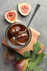 Jar of tasty sweet jam, fresh figs and green leaf on grey table, flat lay