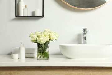 Beautiful roses and bath accessories near sink in bathroom