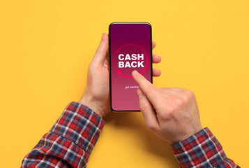 Man using smartphone with word Cashback on orange background, top view