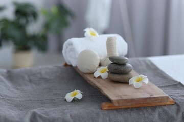 Fototapeta na wymiar Stacked spa stones, flowers, herbal bags and towel on massage table indoors