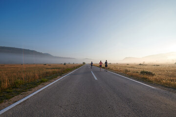 A group of friends, athletes, and joggers embrace the early morning hours as they run through the misty dawn, energized by the rising sun and surrounded by the tranquil beauty of nature