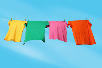 Colorful t-shirts drying on washing line against blue sky, low angle view
