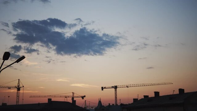 Construction cranes stand idle against the fading light, with scattered clouds painting a soft backdrop.