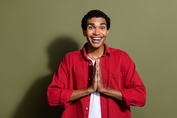 Photo of cheerful excited man dressed red shirt arms together praying isolated green color...