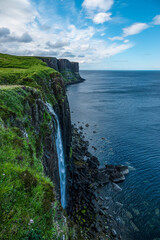 Stunning coastline with high cliffs and waterfall cascading down to rocky shore