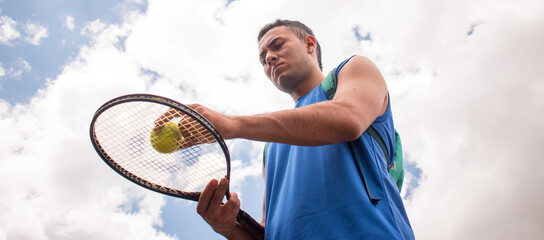 Low angle of man holding tennis racket with tennis balls