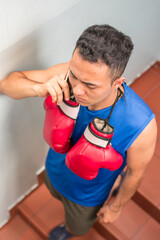 Latin young boxer man training with red boxing gloves on shoulders leaving gym