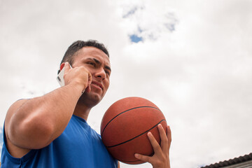 Low angle of Man holding basketball ball and talking phone in court at summer 