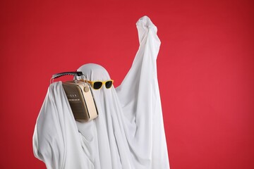 Person in ghost costume and sunglasses using retro radio receiver on red background, space for text