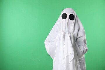Creepy ghost. Person covered with white sheet on green background, space for text