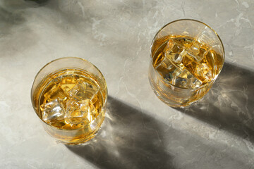 Whiskey with ice cubes in glasses on grey marble table, above view