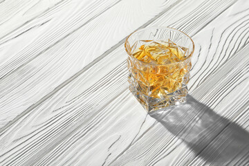 Whiskey with ice cubes in glass on white wooden table, space for text
