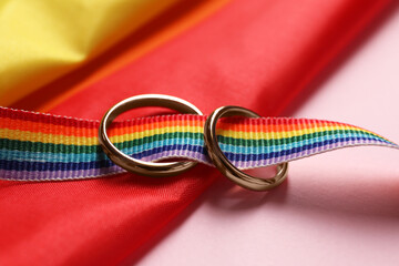Rainbow LGBT flag and wedding rings on pink background, closeup