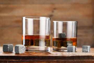 Whiskey stones and drink in glasses on wooden table, closeup
