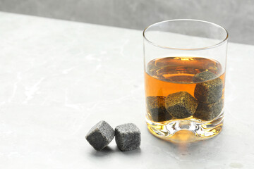 Whiskey stones and drink in glass on light marble table, closeup. Space for text