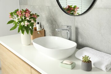 Vase with beautiful Alstroemeria flowers and toiletries near sink in bathroom