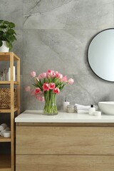 Vase with beautiful pink tulips and toiletries near sink in bathroom