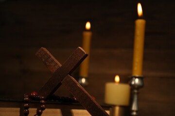 Wooden cross, Bible, rosary beads and church candles against blurred background, space for text