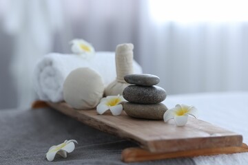 Stacked spa stones, flowers, herbal bags and towel on massage table indoors