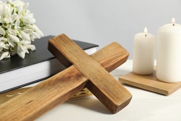 Wooden cross, ecclesiastical books, church candles and flowers on white table, closeup