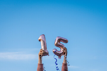 Girl holding 15 years balloons over head outdoors