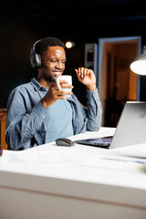 African american guy solving economy tasks online, having fun listening to podcast on headset at home. Male freelancer working on global management strategy with capital funds investments.