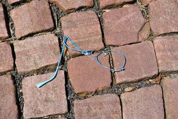 Closeup crushed glasses with broken frame on rough basalt texture of old medieval stone road, brown...