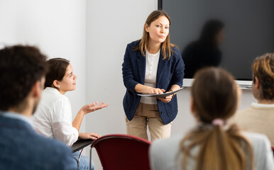 Confident female trainer talking to group of people, brainstorming, discussing ideas in auditory